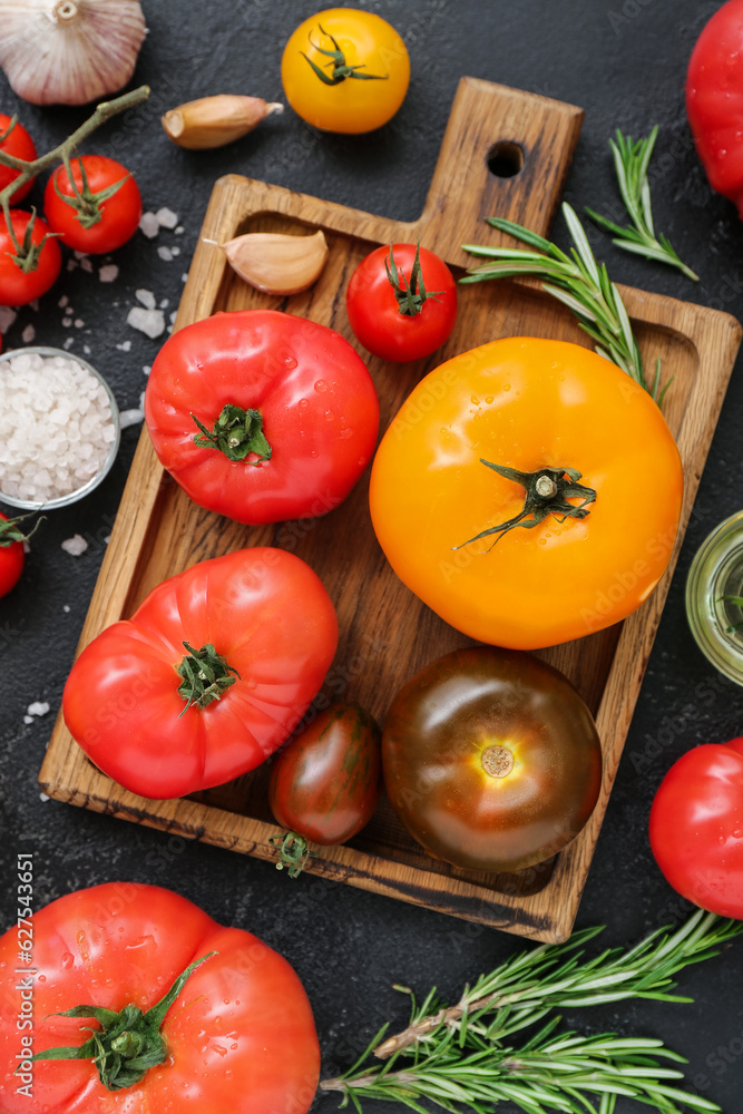 Board with different fresh tomatoes on black background