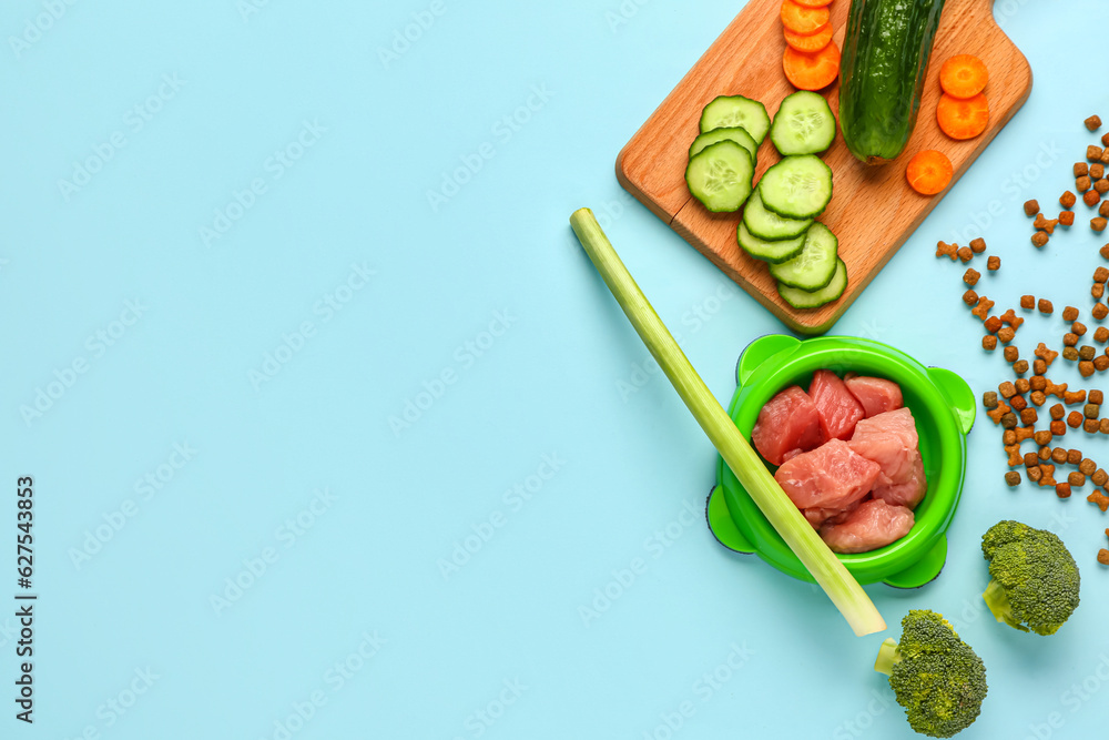 Composition with dry pet food, raw meat and natural products on blue background