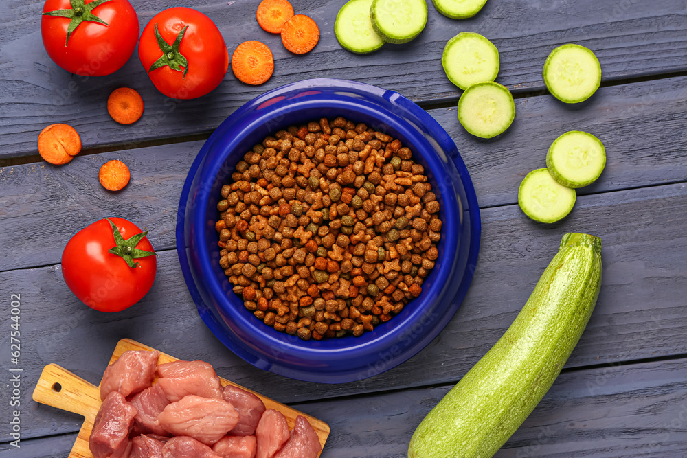 Composition with dry pet food, raw meat and natural products on color wooden background