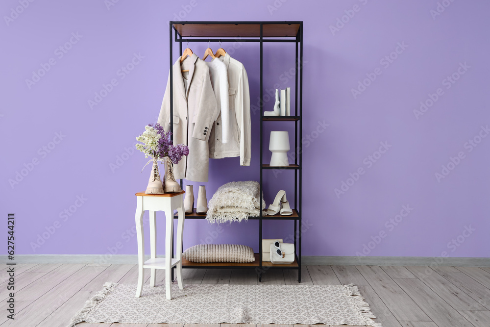 Interior of stylish room with shelving unit, clothes and stool