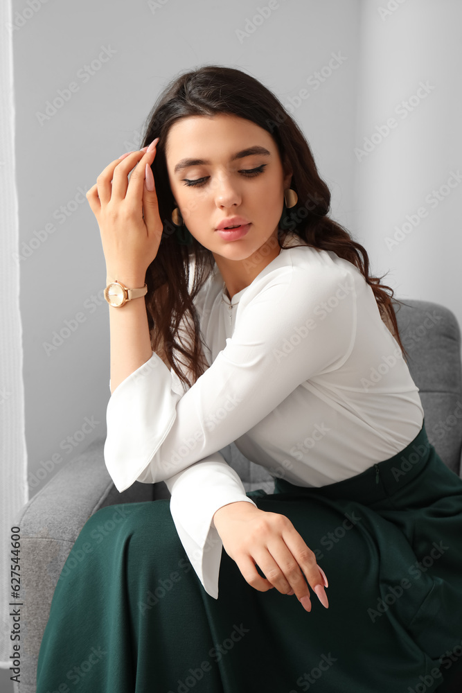 Beautiful young woman with wristwatch sitting on armchair in room