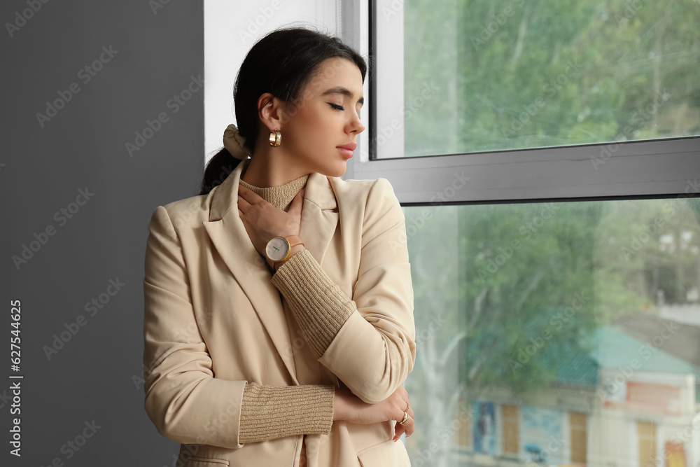 Beautiful young woman with wristwatch near window in room