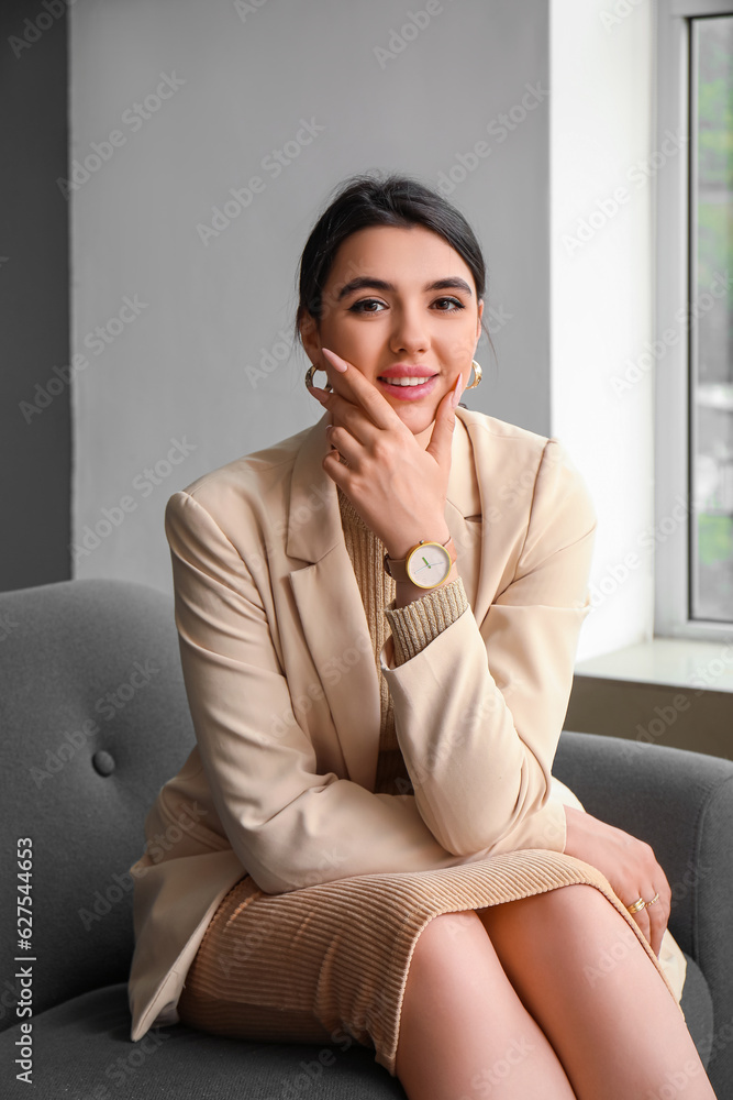 Beautiful young woman with wristwatch sitting on sofa in living room