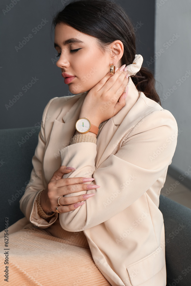 Beautiful young woman with wristwatch sitting on sofa in living room