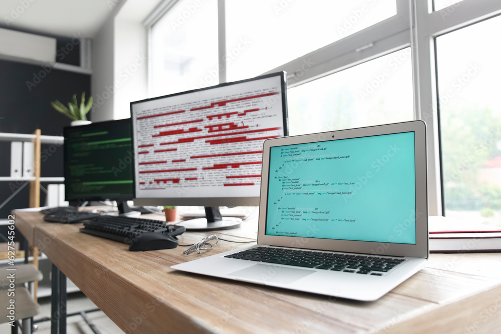 Computer monitor and laptop with programming code at programmers workplace in office, closeup