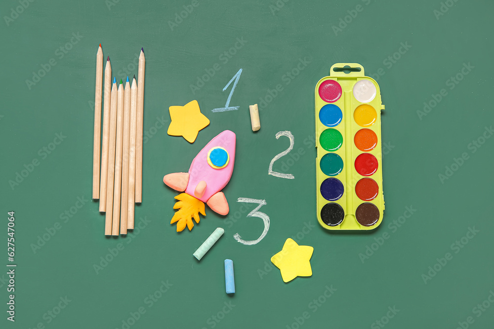 Rocket made of plasticine with different stationery on green chalkboard