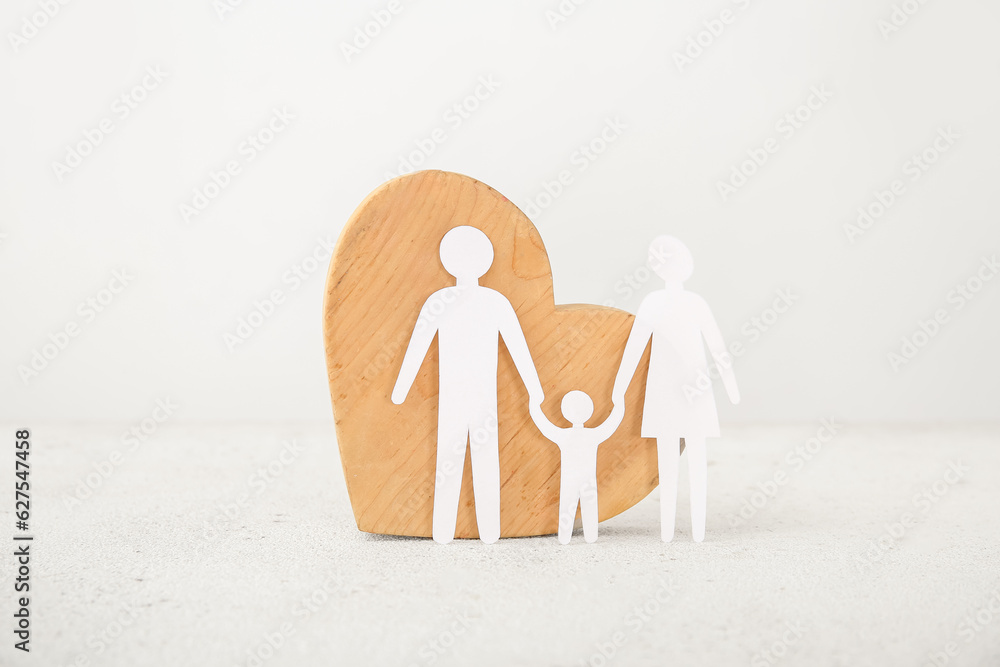 Wooden heart with figures of family on white table. Family love concept