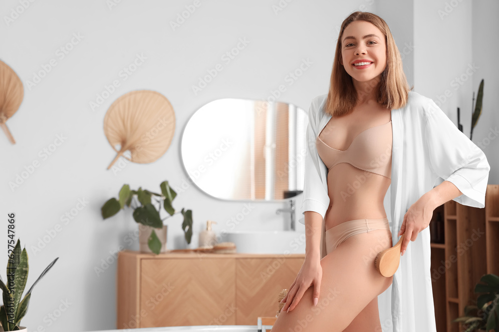 Young woman massaging her buttocks with anti-cellulite brush in bathroom