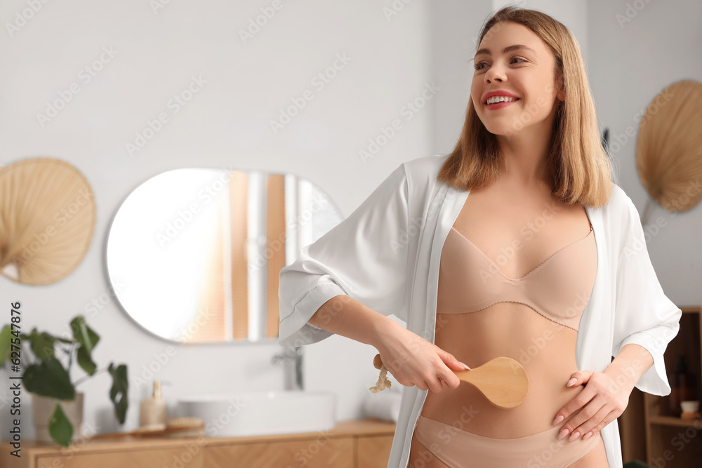 Young woman massaging her belly with anti-cellulite brush in bathroom