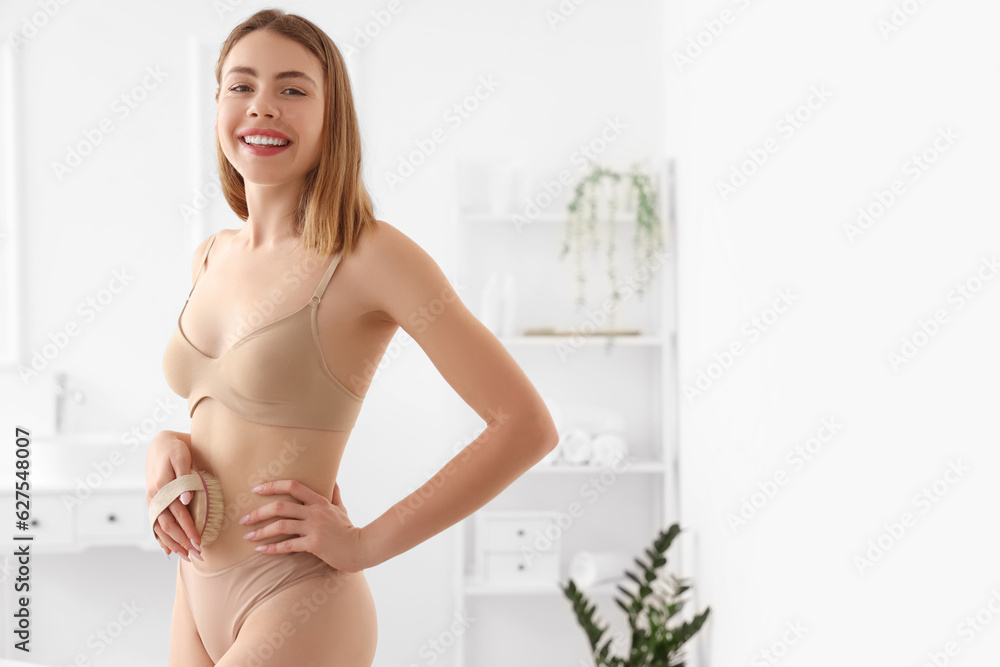 Young woman massaging her belly with anti-cellulite brush in bathroom