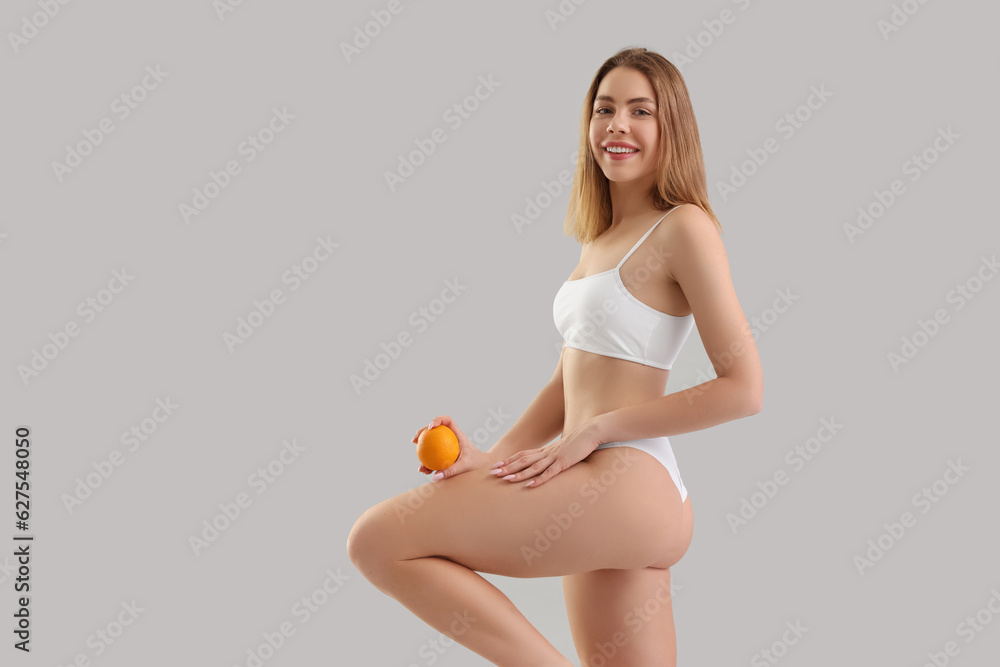 Young woman with cellulite problem and orange on light background