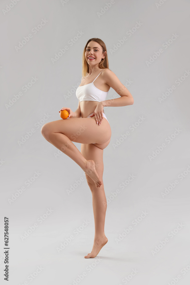 Young woman with cellulite problem and orange on light background