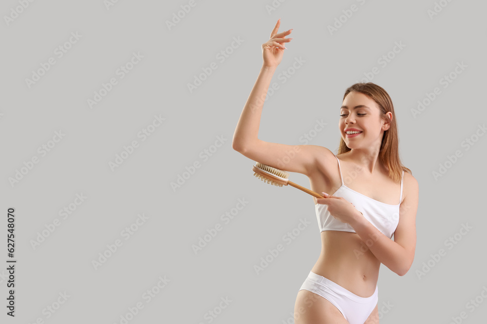 Young woman massaging her arm with anti-cellulite brush on light background