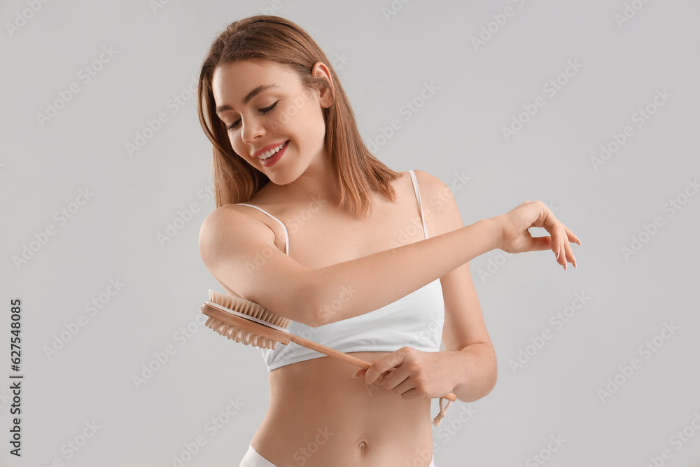 Young woman massaging her arm with anti-cellulite brush on light background