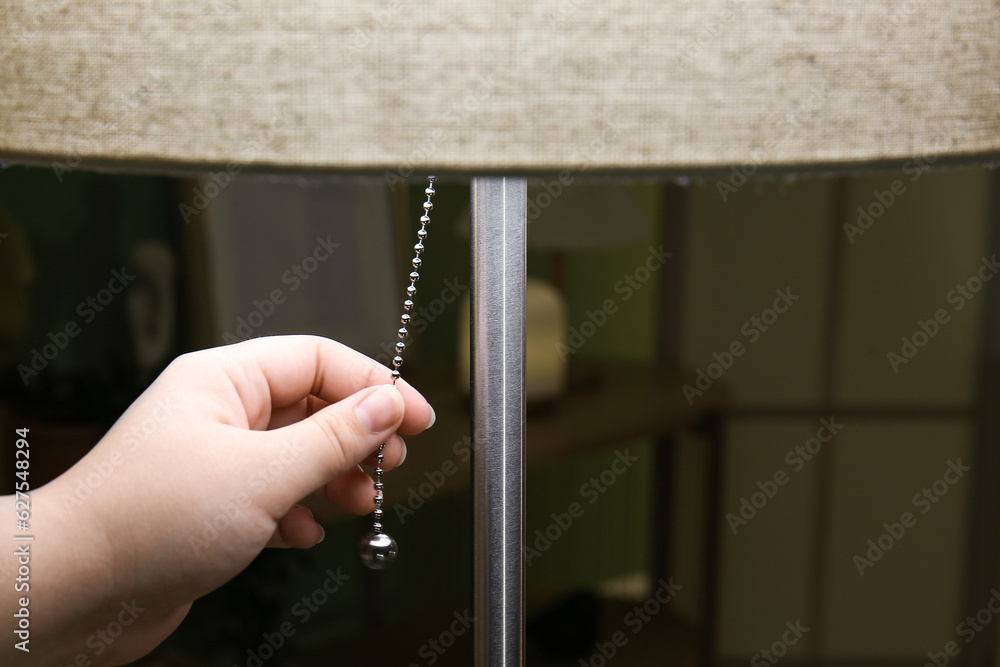 Woman turning on floor lamp in dark living room, closeup