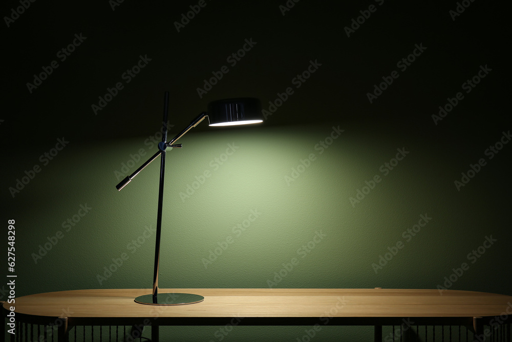 Glowing lamp on wooden table in dark room