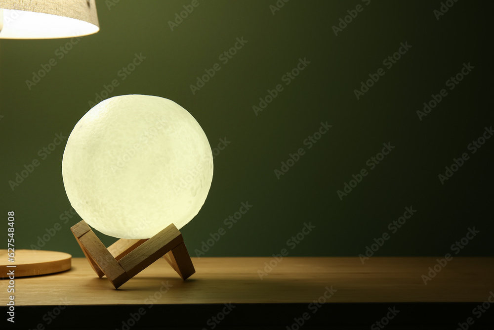 Glowing lamp in shape of moon on wooden table in dark room, closeup