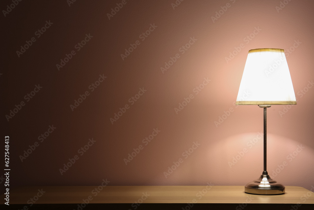 Glowing lamp on wooden table in dark room