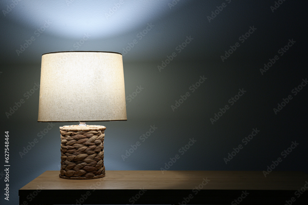 Glowing lamp on wooden table in dark room