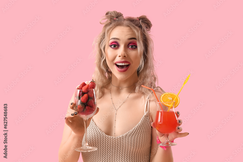 Young woman in swimsuit with cocktail and strawberries on pink background