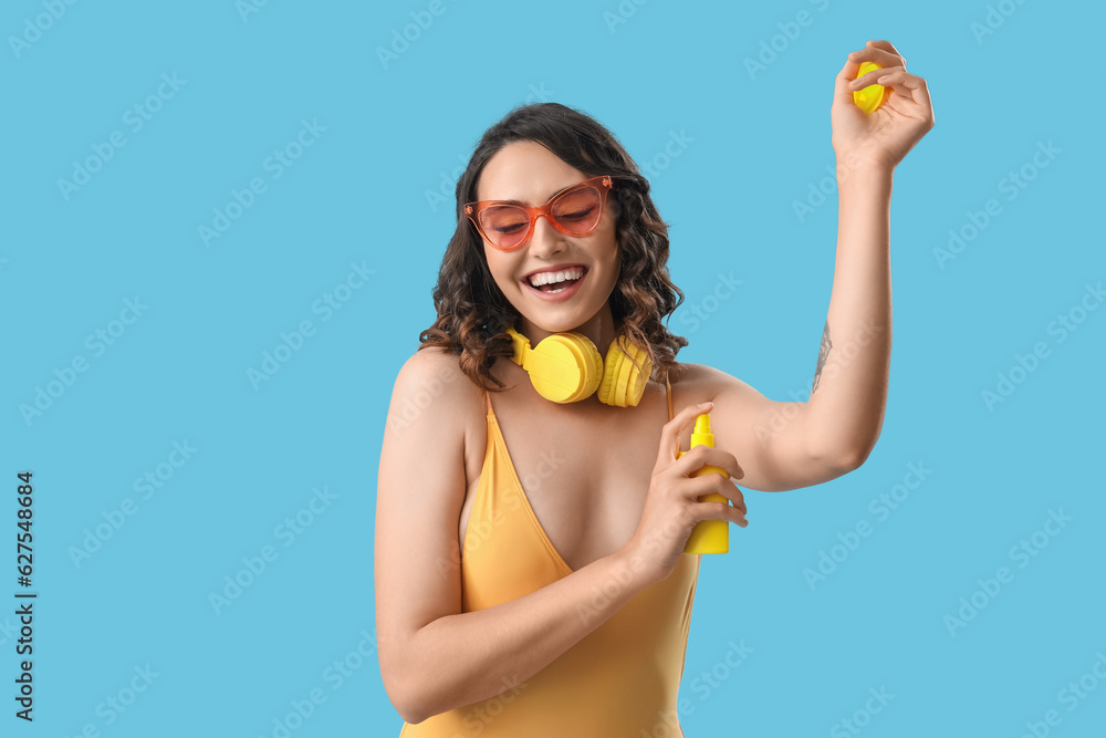 Young woman in swimsuit applying sunscreen cream on blue background