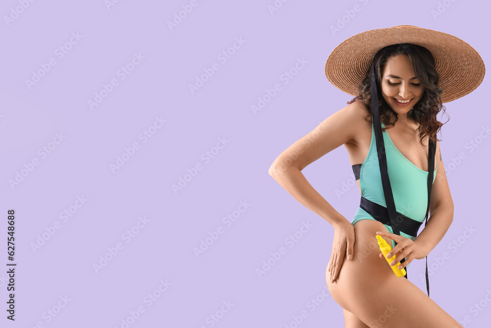 Young woman in swimsuit with sunscreen cream on lilac background