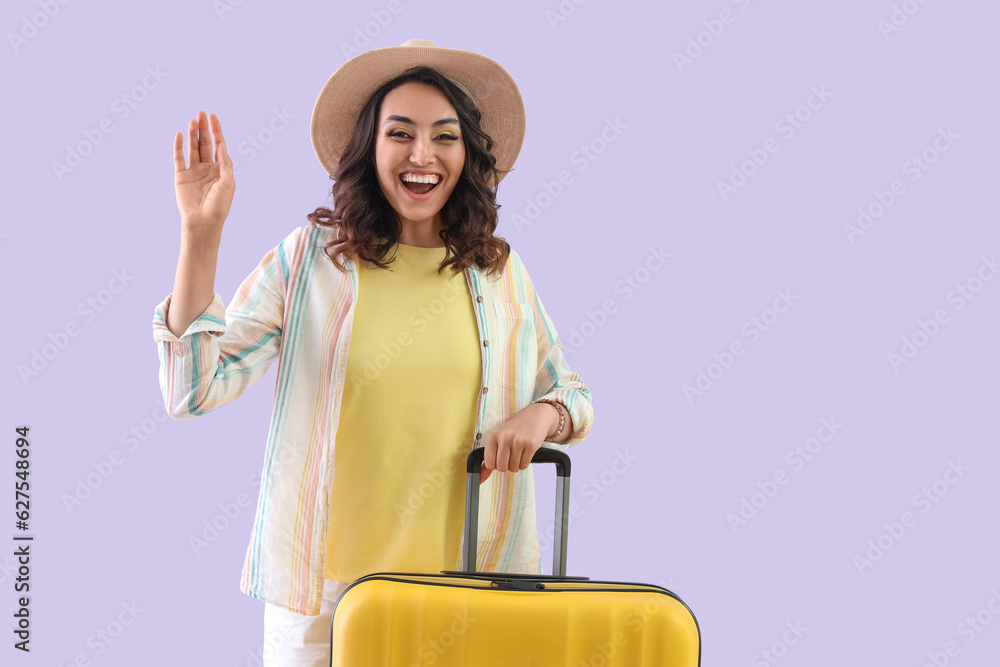 Young woman in summer hat with suitcase on lilac background