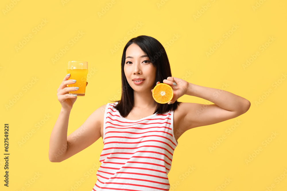 Beautiful Asian woman with orange and glass of juice on yellow background