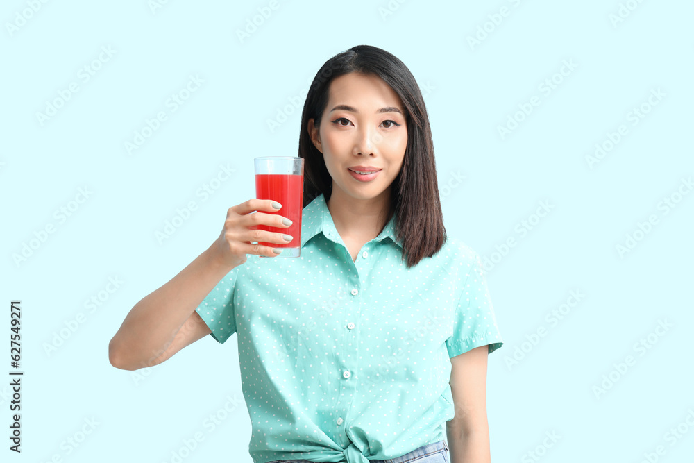 Beautiful Asian woman with glass of cherry juice on blue background