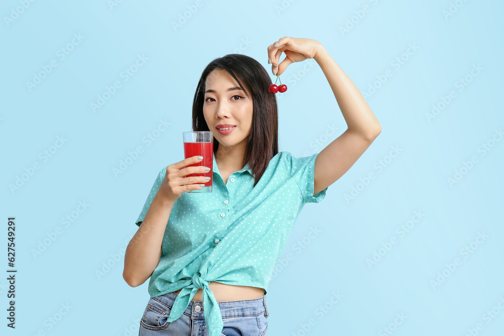 Beautiful Asian woman with cherry and glass of juice on blue background