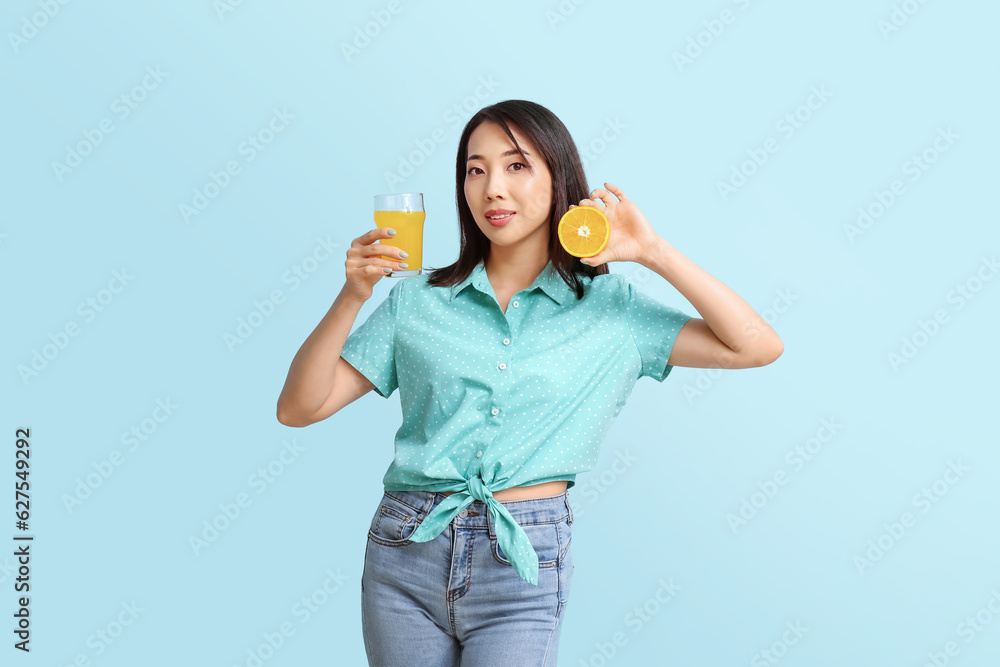 Beautiful Asian woman with orange and glass of juice on blue background