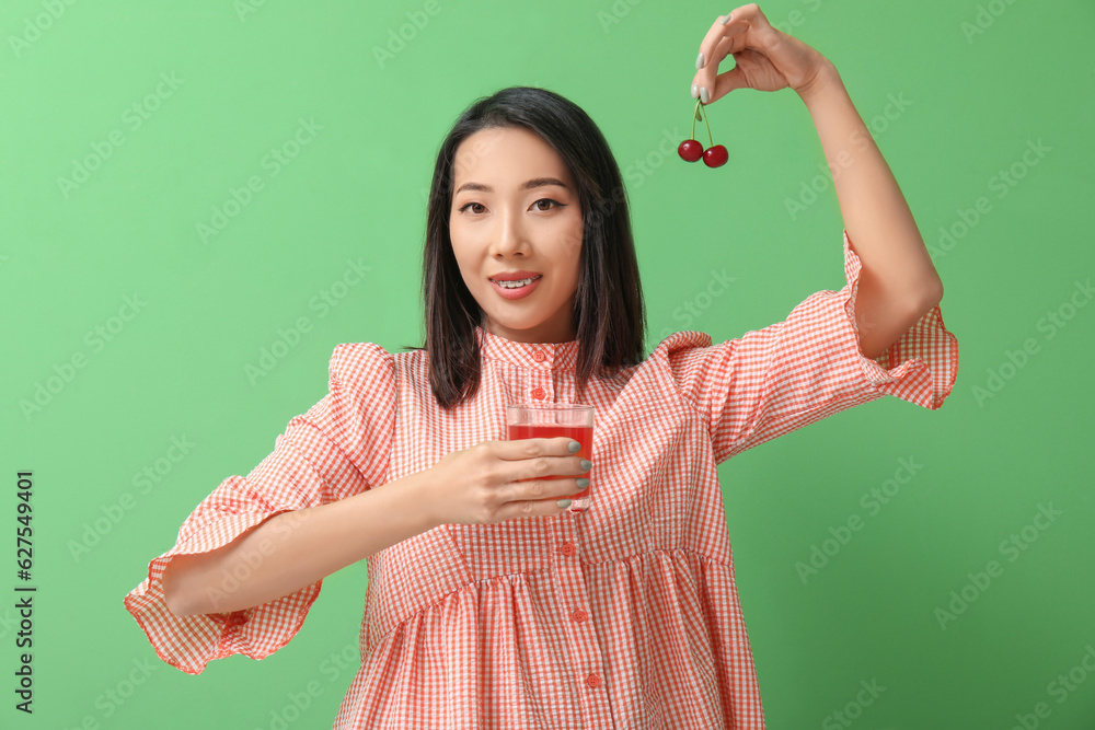 Beautiful Asian woman with cherries and glass of juice on green background