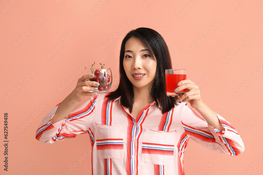 Beautiful Asian woman with cherries and glass of juice on pink background