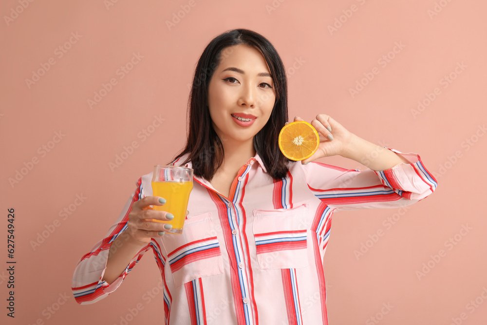 Beautiful Asian woman with orange and glass of juice on pink background