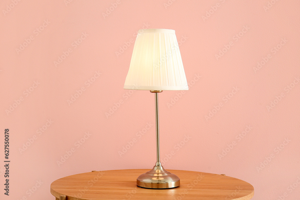 Glowing lamp on wooden table near pink wall