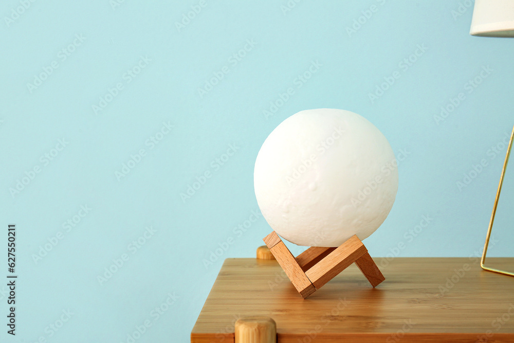 Moon shaped lamp on wooden table near blue wall