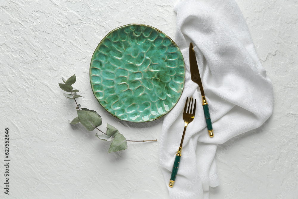 Table setting with clean plate, cutlery and eucalyptus branch on grey background