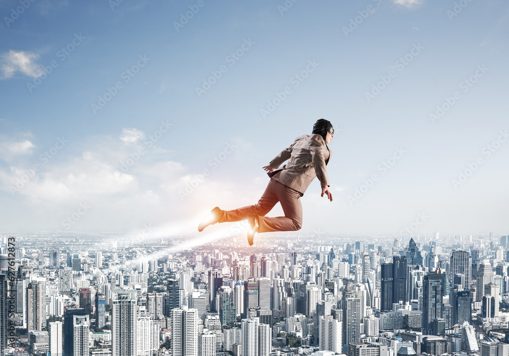 Businessman in suit and aviator hat flying in sky