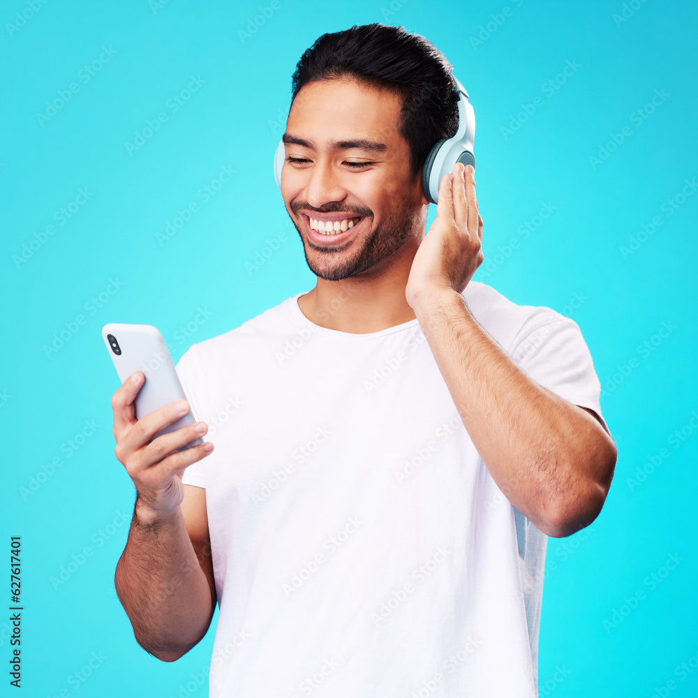 Headphones, music and Asian man with smartphone for listening in studio isolated on a blue backgroun