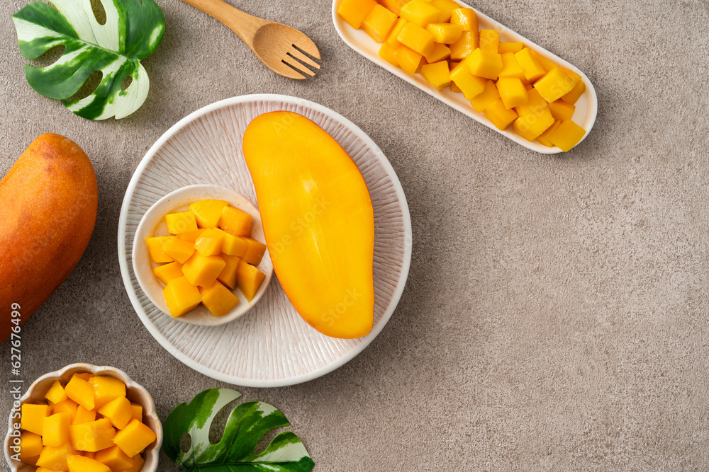 Fresh chopped, diced mango cubes on gray table background with tropical leaf.