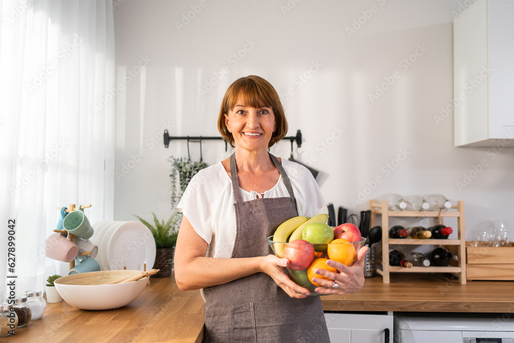 Portrait of Caucasian elderly woman hold fruit bowl and look at camera. 