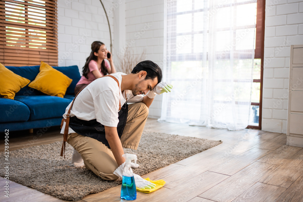 Asian young man cleaning house indoors following order from his wife. 