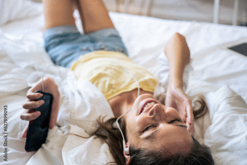 Caucasian young woman listen to music while lying down on bed in house. 