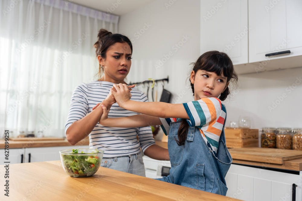 Caucasian mother teach and motivate young daughter eat green vegetable. 