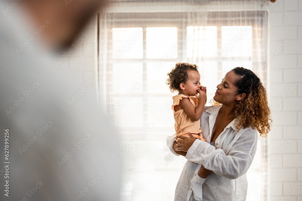 African American mother holding young baby girl in living room at home. 