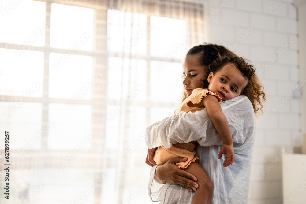 African American mother holding young baby girl in living room at home. 