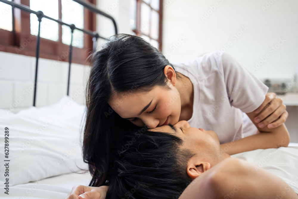 Asian wife kissing her husband while lying down sleep on bed in bedroom. 