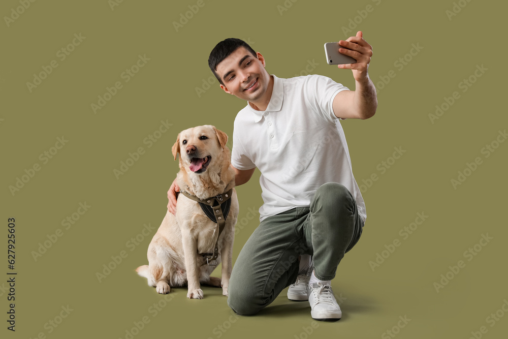 Young man with mobile phone and Labrador dog taking selfie on green background