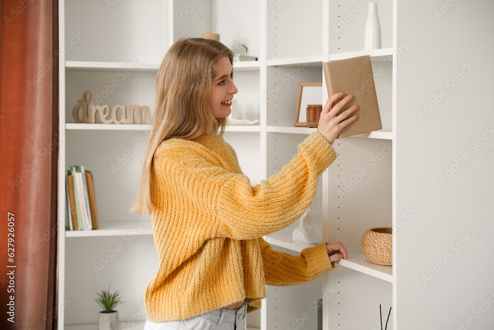 Young woman taking book from shelf at home