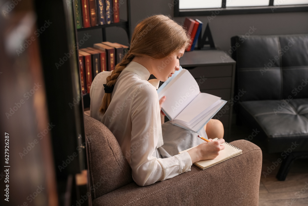 Young businesswoman reading book and making notes in office